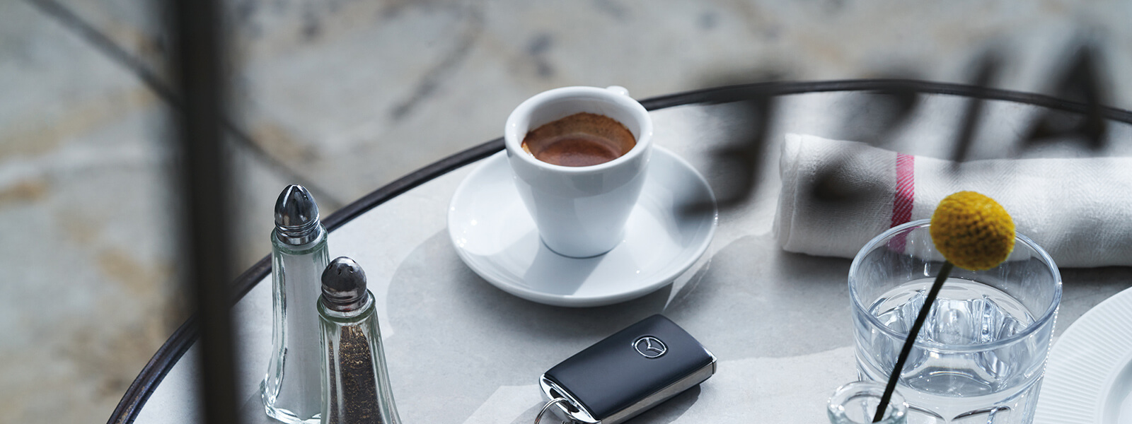 Overhead view of table with salt and pepper shakers, pastry, cup of coffee, and a set of Mazda keys.