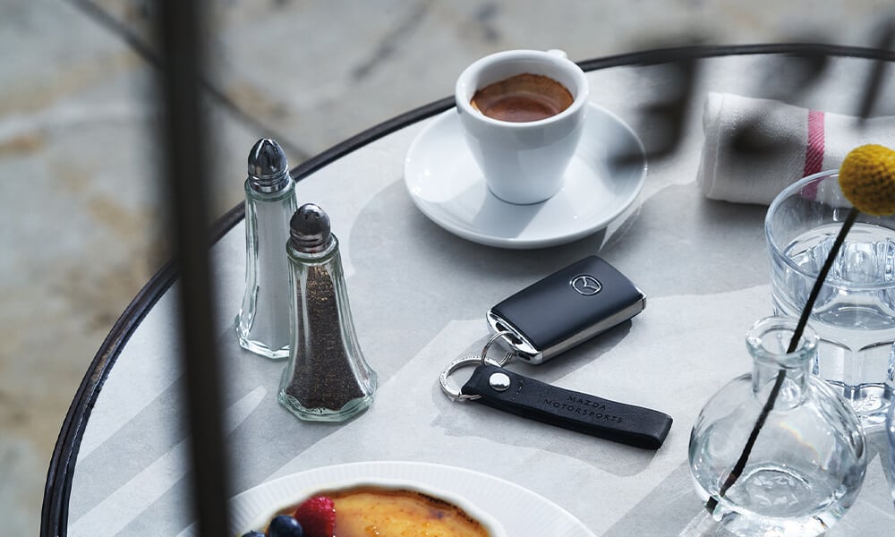 Overhead view of table with salt and pepper shakers, pastry, cup of coffee, and a set of Mazda keys.