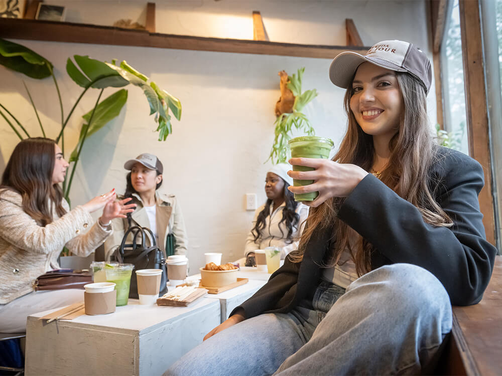 Four people sit around a table smiling and drinking coffee while wearing Mazda Coffee Tour hats.