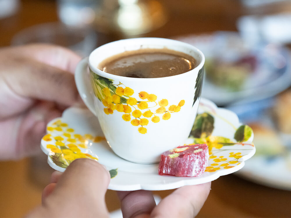 Close-up view of hands holding coffee in a matching cup and saucer decorated with flowers.