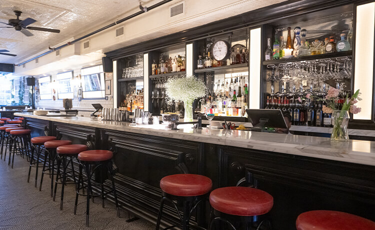 A view of the bar Café Renée Bar with stools, bottles, and flowers visible. 
