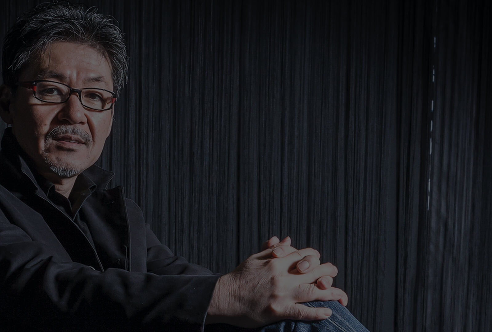 Shaded portrait of Ikuo Maeda sitting with hands folded on desk