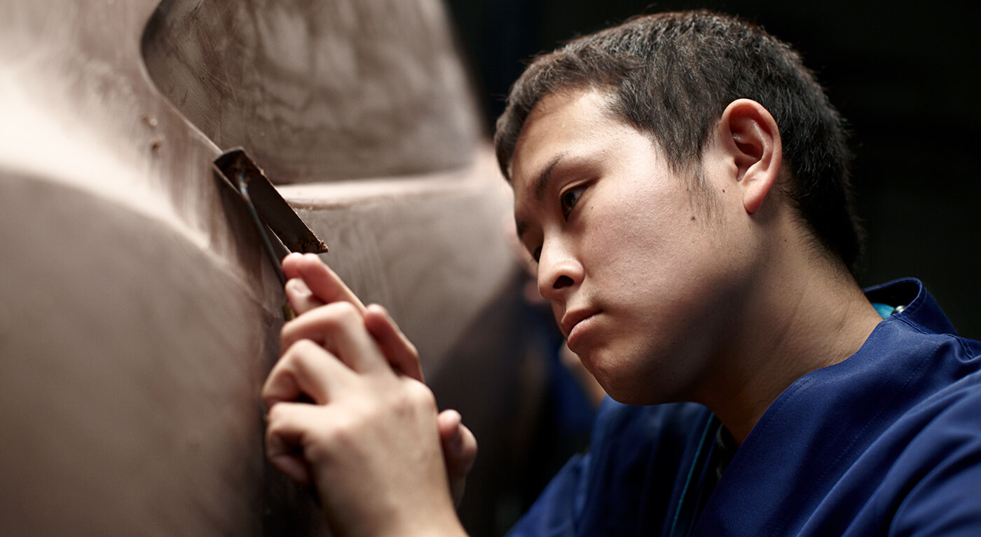Artisan in blue coveralls concentrates intently as he shapes a clay form. 