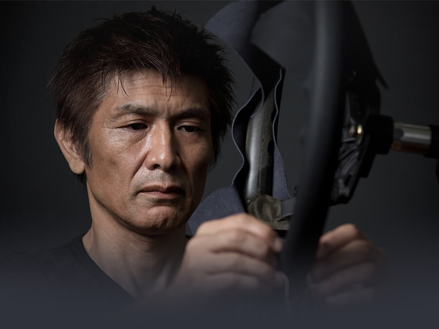 Mazda upholsterer adjusts fabric on steering wheel. 