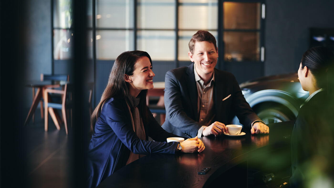 Smiling young professional couple enjoy coffee while speaking with a Mazda retailer