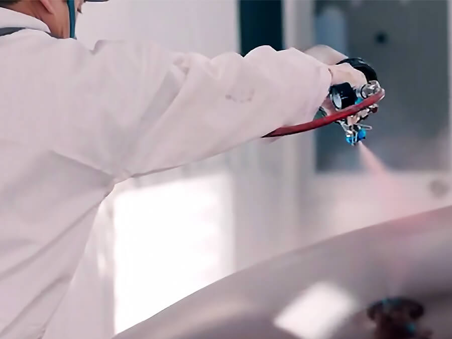 A Mazda technician seen from behind spraying paint onto a Mazda car hood.