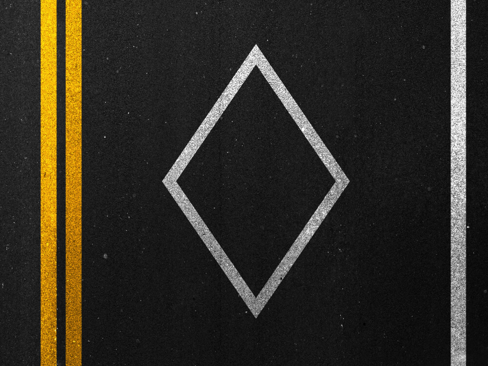 View from slightly above highway asphalt featuring yellow painted lines and HOV diamond. 