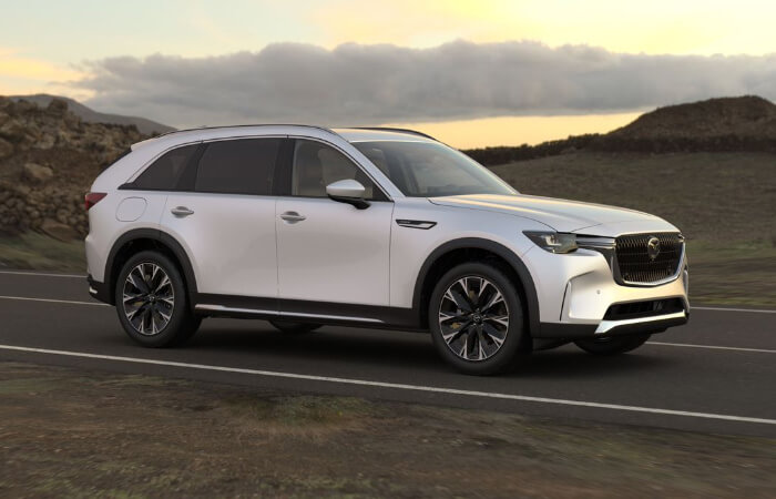 CX-90 PHEV drives down secluded dusty highway at sun down.  