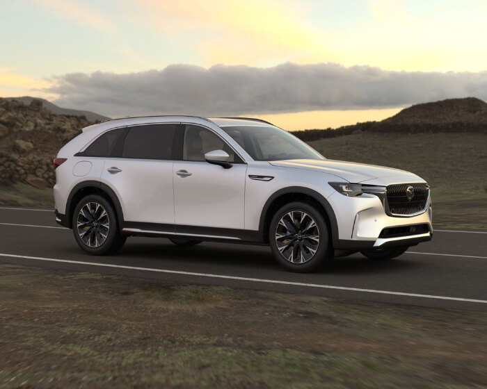 CX-90 PHEV drives down secluded dusty highway at sun down. 
