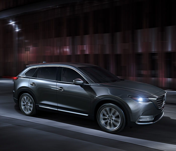 Grey Mazda SUV driving along urban street at night.