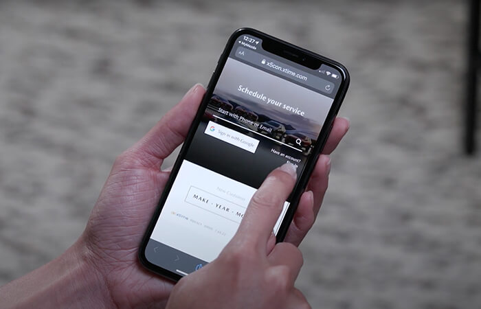Hands hold smartphone with MyMazda app open, swiping through features.  