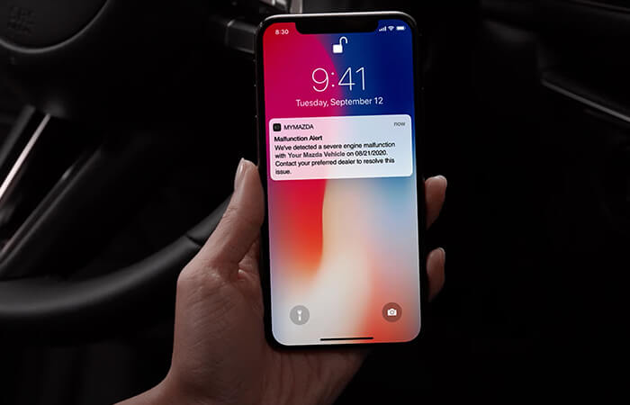 Hand holding smartphone displaying lock screen with MyMazda notification.  