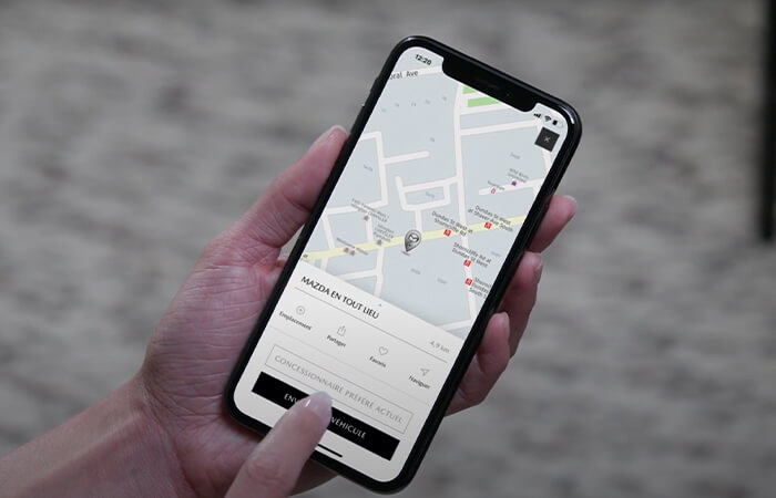 Des mains qui tiennent un téléphone intelligent avec l’appli MyMazda ouverte et parcourent les fonctions.   