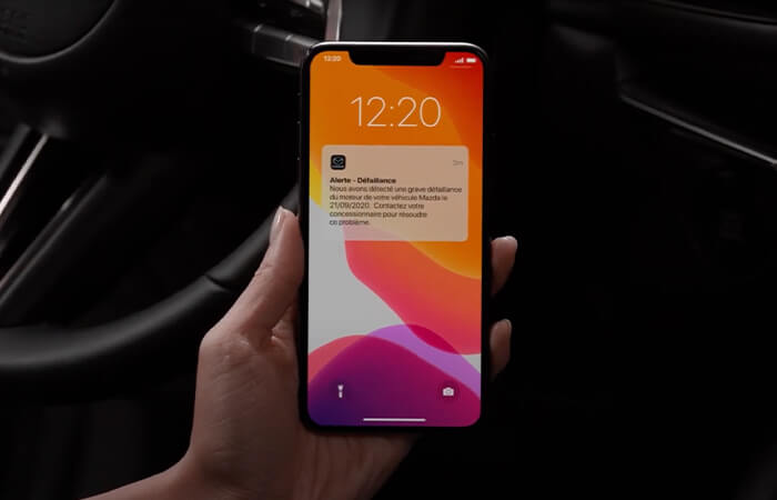Une main tient un téléphone intelligent affichant l’écran de verrouillage avec une notification MyMazda. 