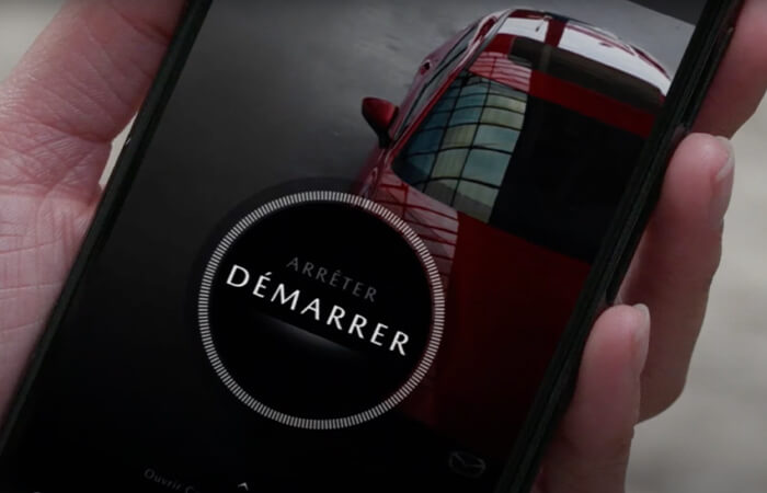 Une main tient un téléphone intelligent avec l’applin MyMazda affichant le bouton de démarrage.   