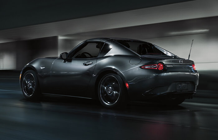 Polymetal Grey Metallic Mazda MX-5 RF hardtop driving along dimly lit urban street.