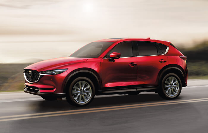 Soul Red Crystal Mazda SUV drives along rural highway with brown hill country blurred in the background. 
