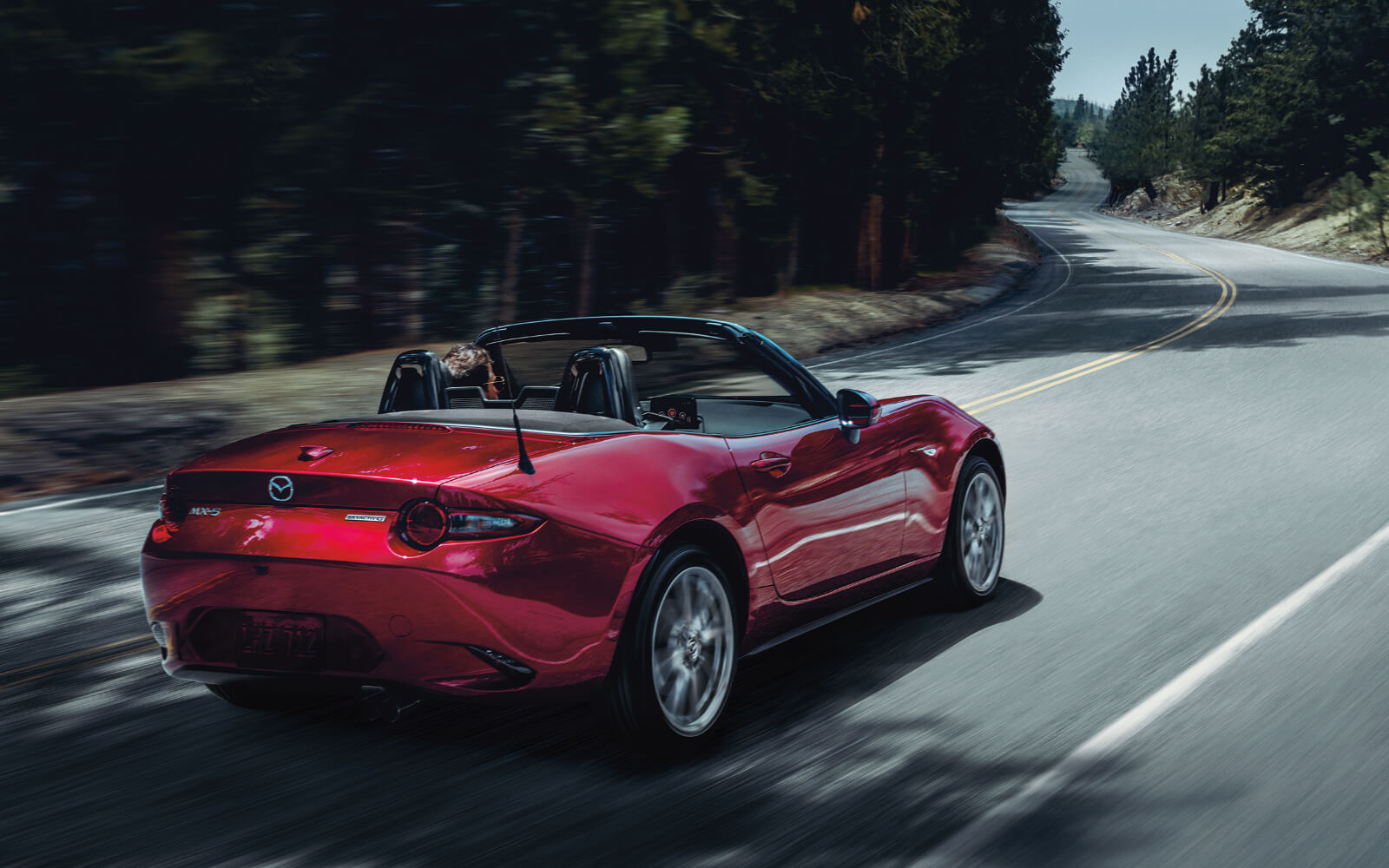 Soul Red Mazda MX-5 Soft Top 2-Seat Convertible rounding a highway curve on a sunny day 