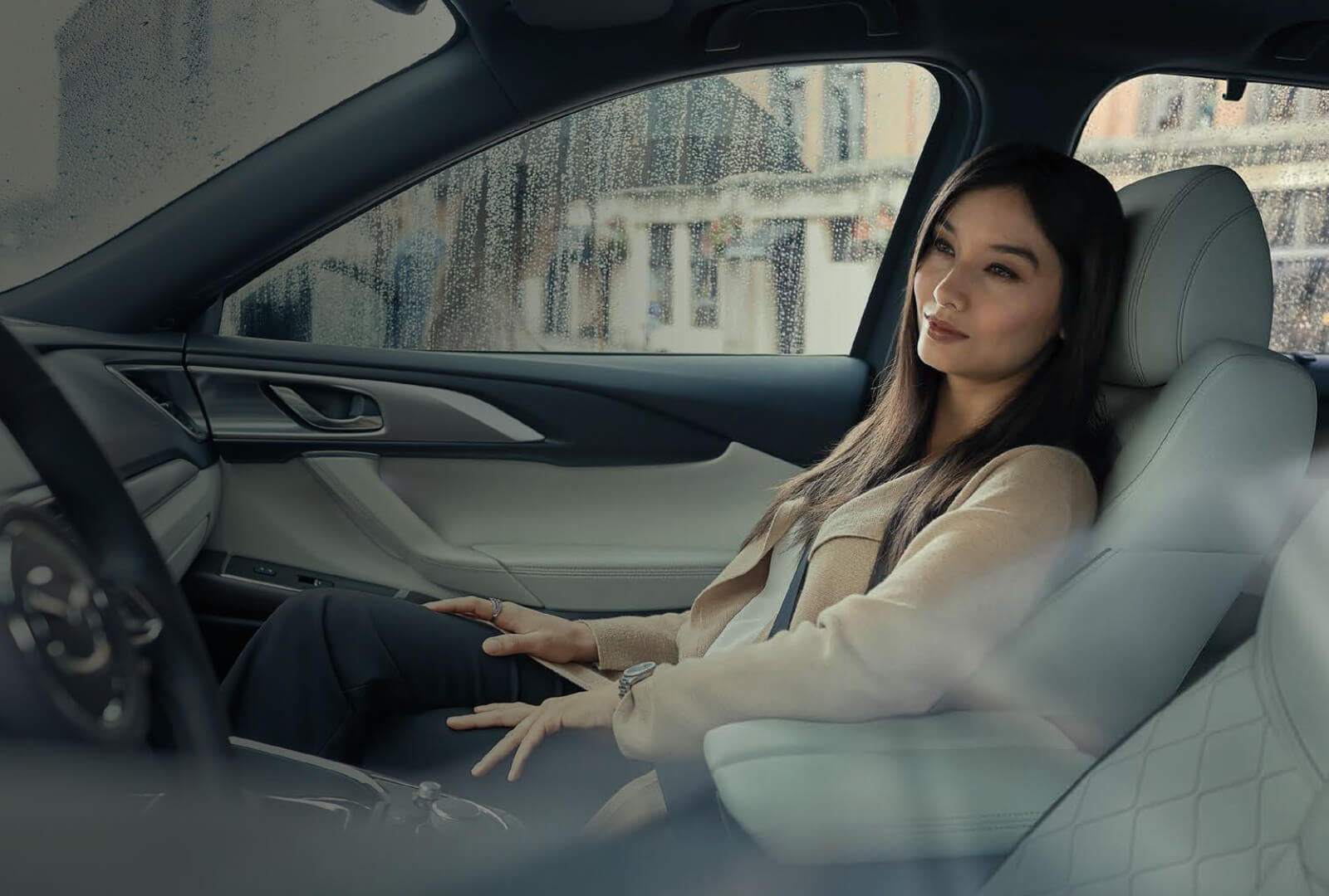 Well-dressed woman seated comfortably in passenger seat of a Mazda CX-9 with rain drops visible on window.