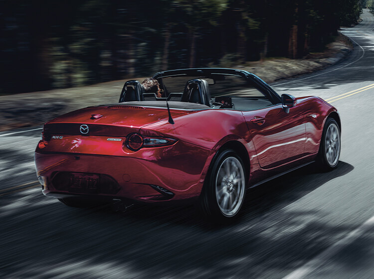 Red Miata with top down taking a curve on a country highway.