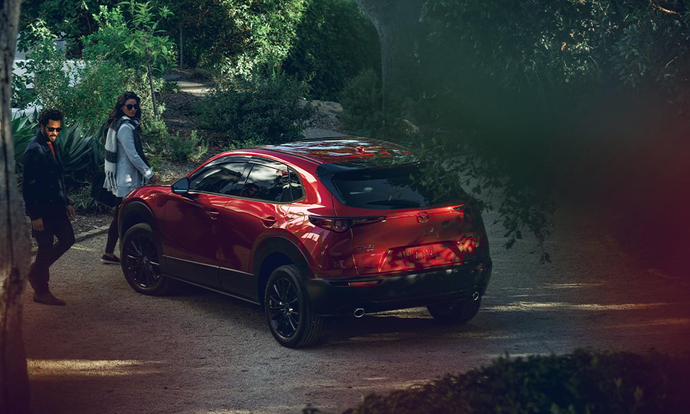 A woman opening the driver side door of a Soul Red Crystal Metallic Mazda CX-30