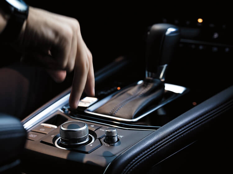 Driver’s hand reaches down to adjust controls on Mazda Connect console next to gear shift.