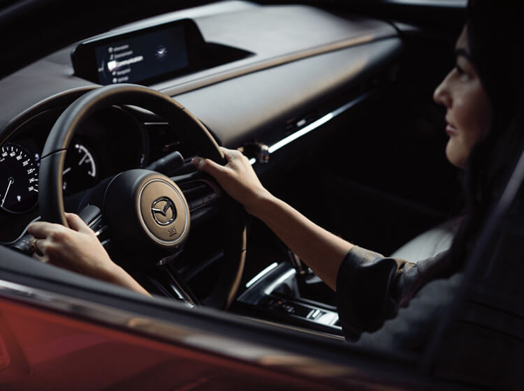 Woman with hands on steering wheel and Mazda Connect display visible in background.