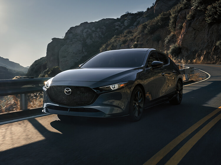 Mazda3 sedan approaches on rural highway after rounding curve with jagged hillside in background