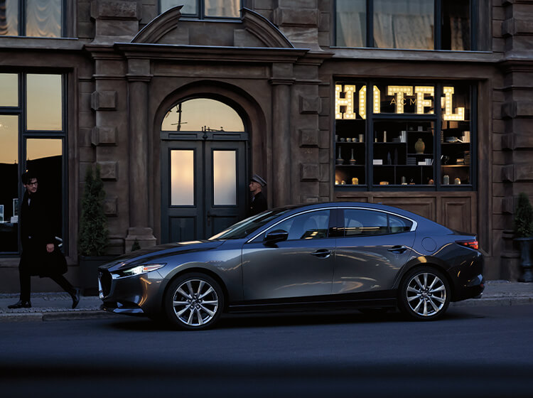 Pedestrian takes a second look as he passes a Mazda sedan parked on city street in front of old hotel 