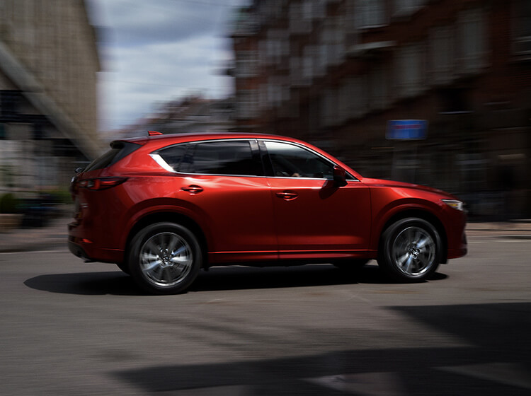 Soul red Mazda SUV driving past blurred buildings 