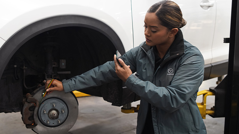 A Mazda technician working on a vehicle's brakes