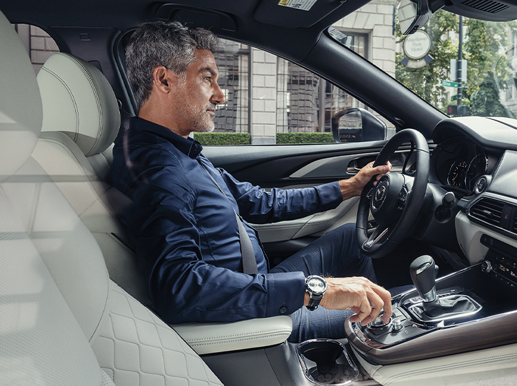 Male professional in blue collared shirt seen from passenger side with left hand on wheel and right hand  adjusting cockpit controls.