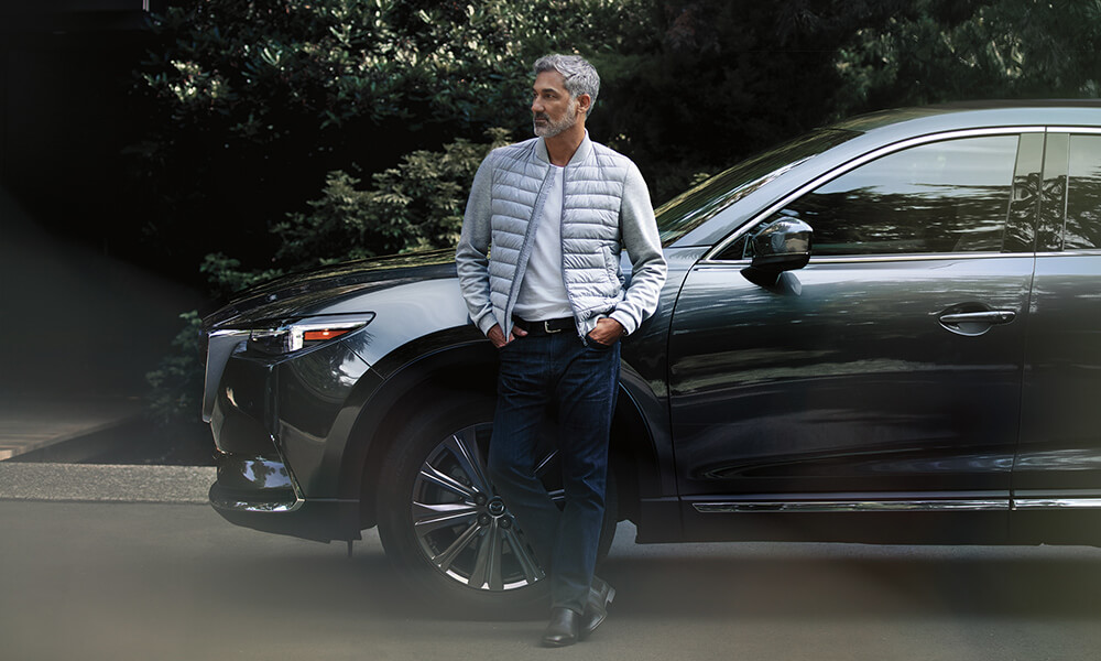 Man leans against driver side front panel of his Mazda SUV