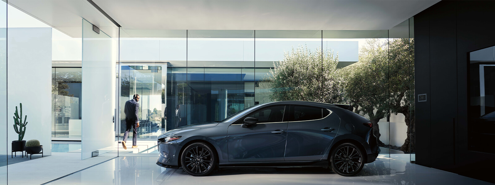 Man in grey suit exiting retailer showroom looks over shoulder at Deep Crystal Blue Mica Mazda3 Sport on display