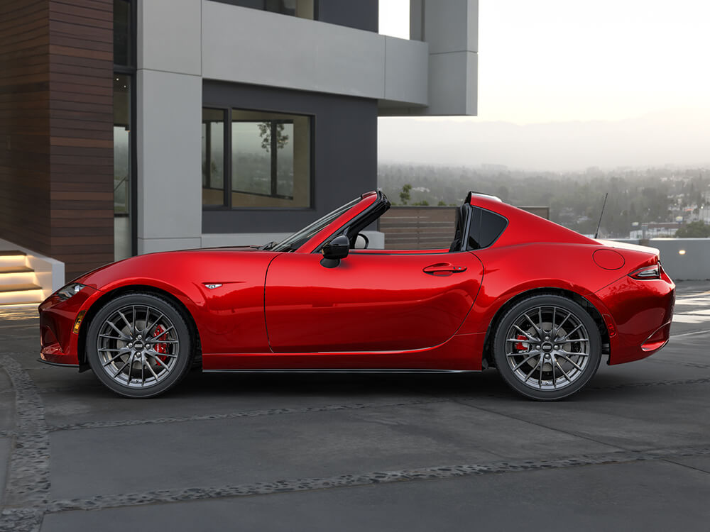 Side view of a red MX-5 RF parked in front of a modern home. 