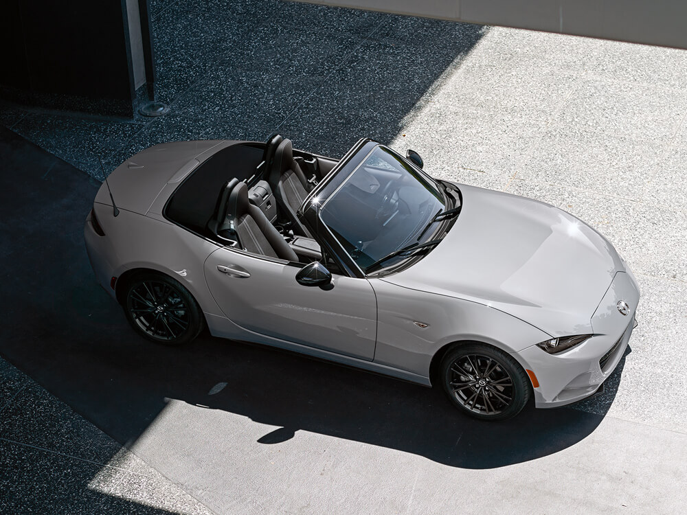 View of a silver MX-5 ST with the top down parked half in sunlight.