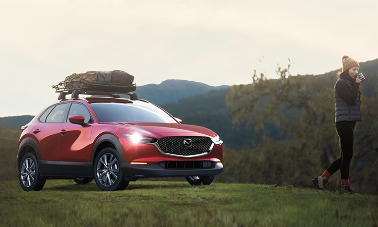 A couple converses behind their CX-30 with rear liftgate open. Dufflebags, cooler, and other items fill the cargo space.