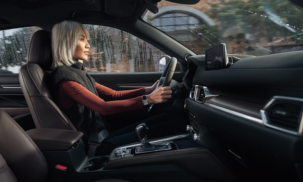 Passenger side view of woman driving in Mazda CX-5 with rain outside window.