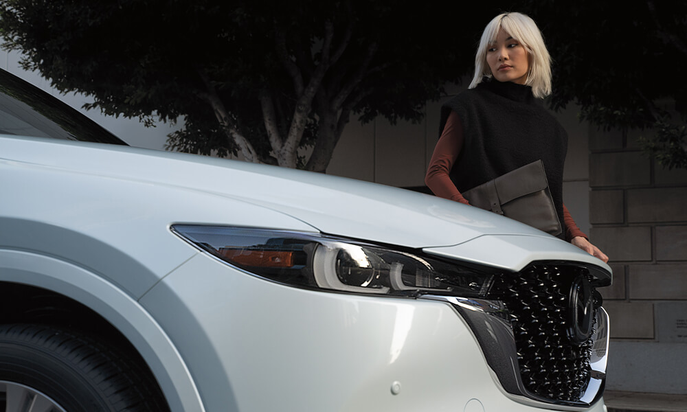 Close up view of Rhodium White Metallic Mazda CX-5 front passenger’s side with woman exiting car.
