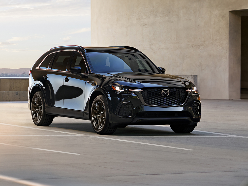 Dark blue CX-70 MHEV parked in a parking lot with smooth stone building in the background.