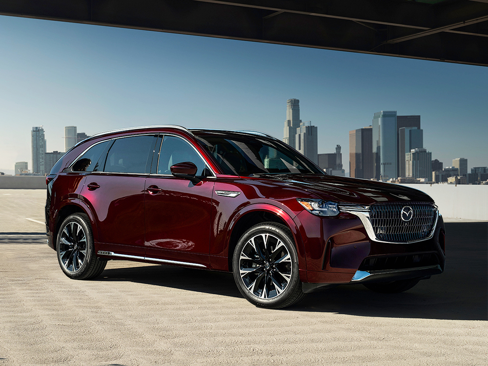 Artisan Red CX-90 MHEV parked across from a city skyline.