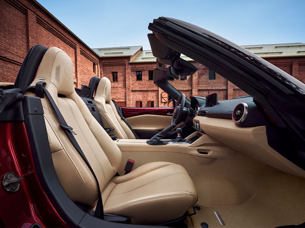 View from the passenger side of the MX-5 ST 35th Anniversary Edition with its top down in front of a building. 