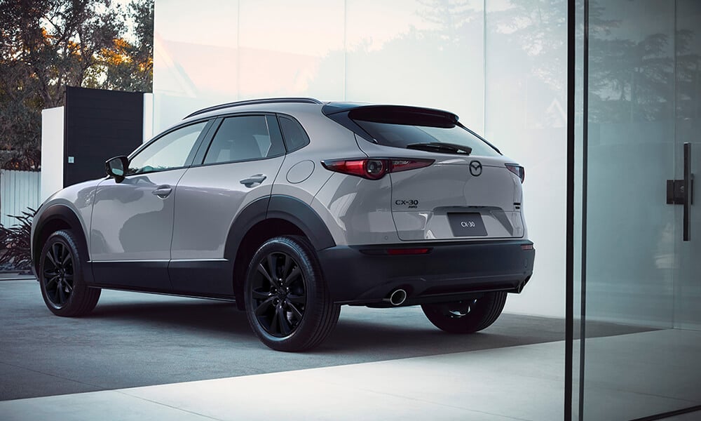 Drivers side rear corner of the Mazda CX-30 parked in a modern driveway with a sliding door in the foreground.