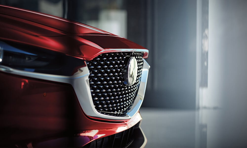Close-up side view of the grille of a Soul Red Crystal Metallic Mazda CX-30, brightly lit.