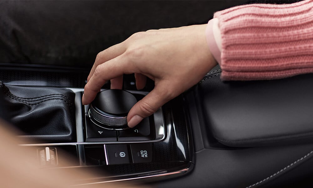 A hand reaches out to the centre console of the Mazda CX-30 adjusting a knob.