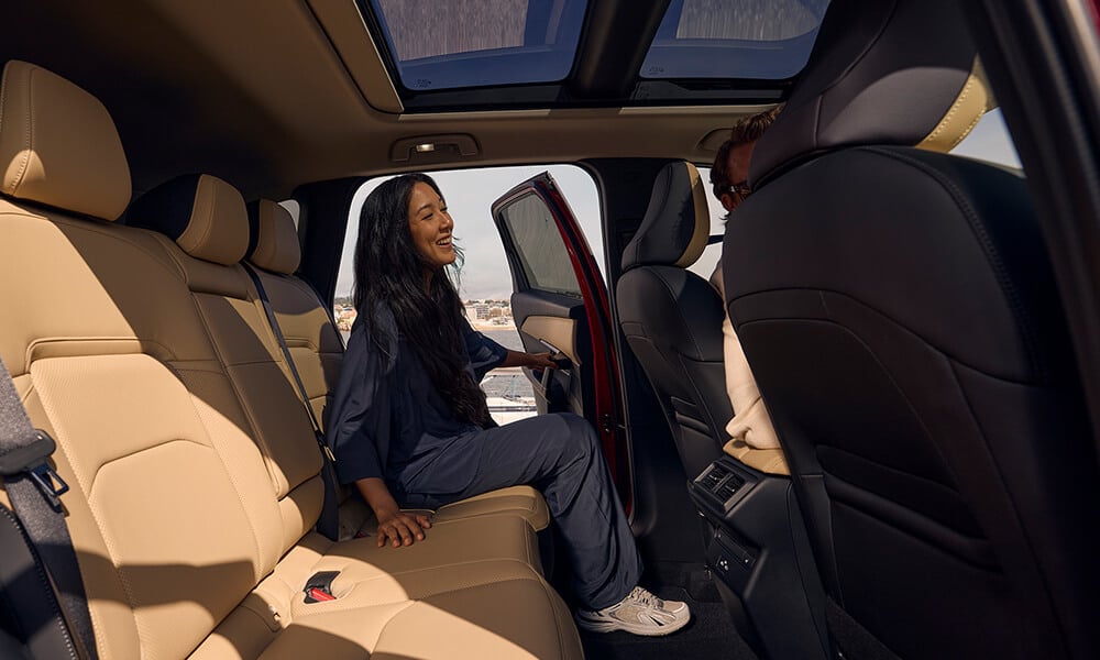 View of the Mazda CX-5 backseats from the passenger-side door, with a woman entering through the driver’s side.