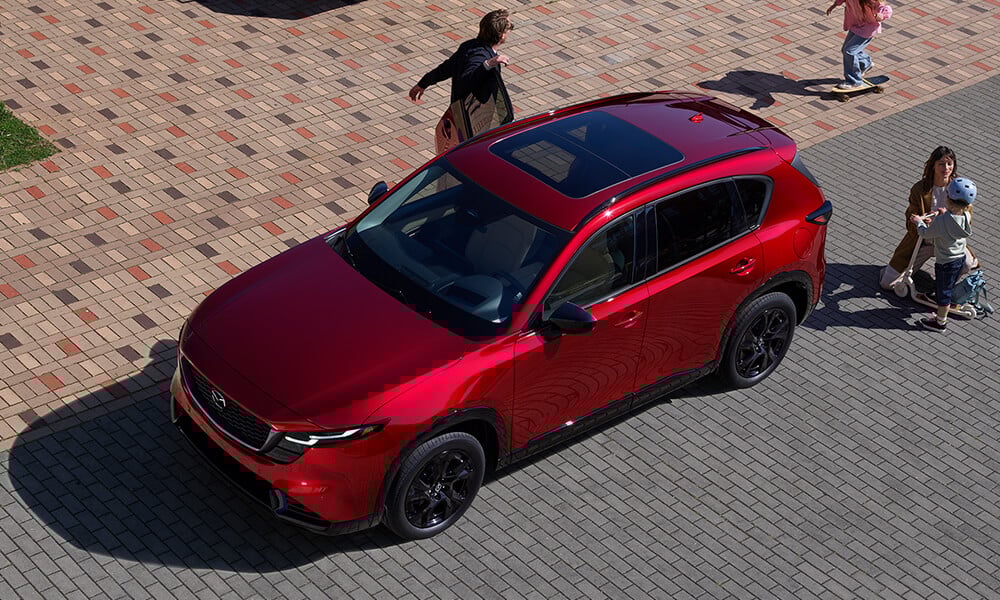 Overhead view of a family gathered around a Soul Red Crystal Metallic Mazda CX-5, with children playing nearby.