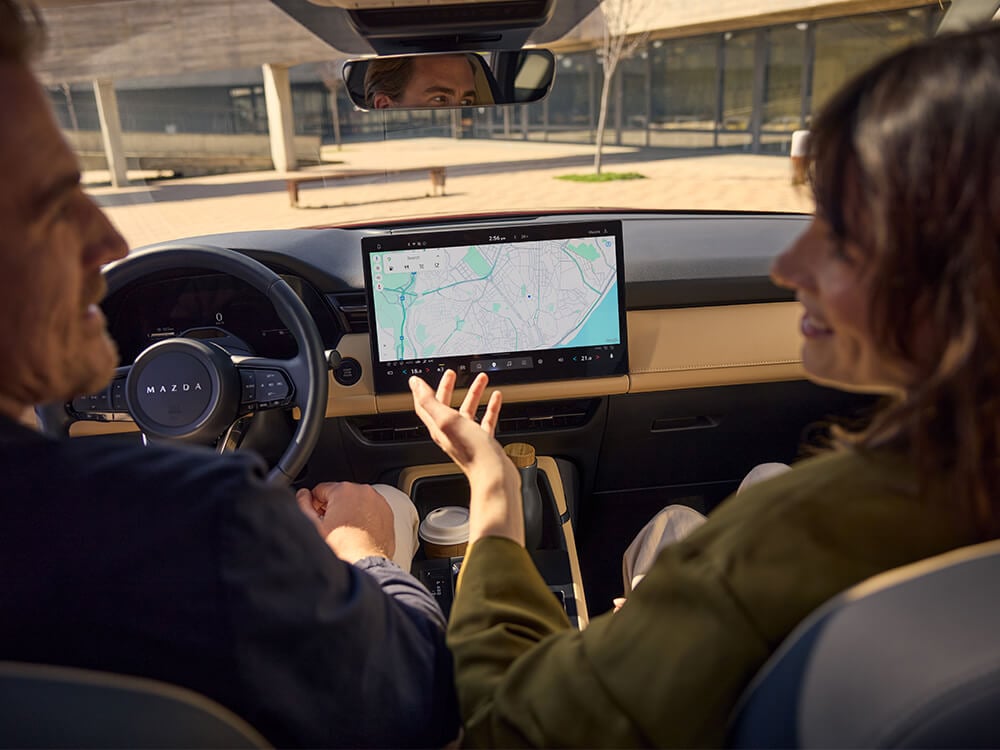 View from behind of two people in the front seats, with the centre display showing Google Maps navigation
