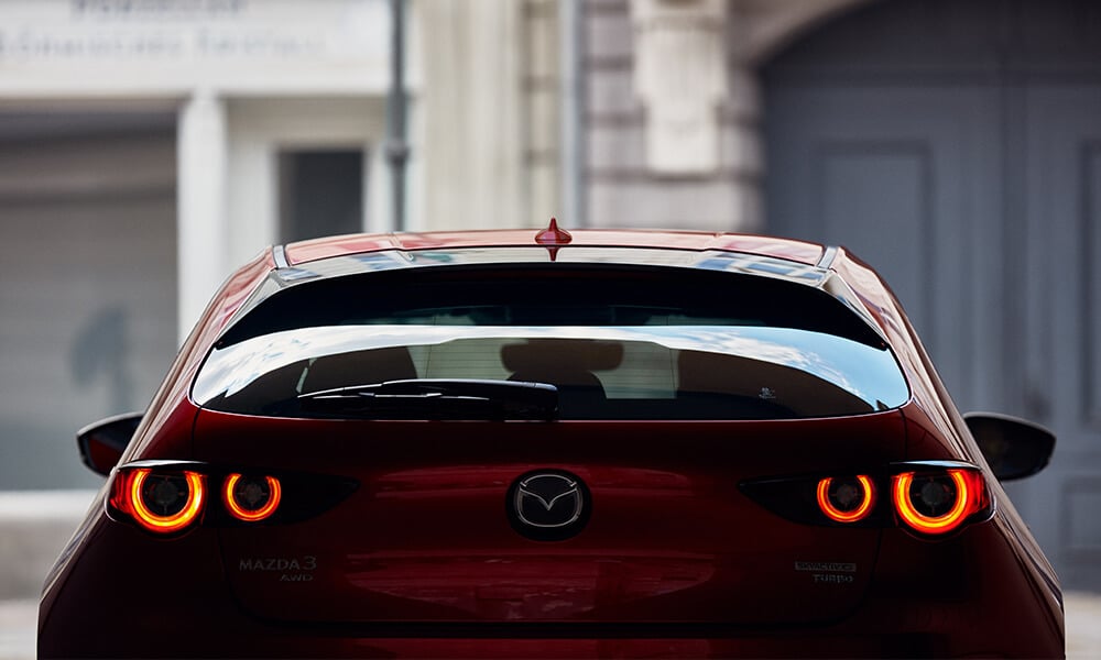 Rear view of a Soul Red Crystal Metallic Mazda3 Sport with taillights illuminated.