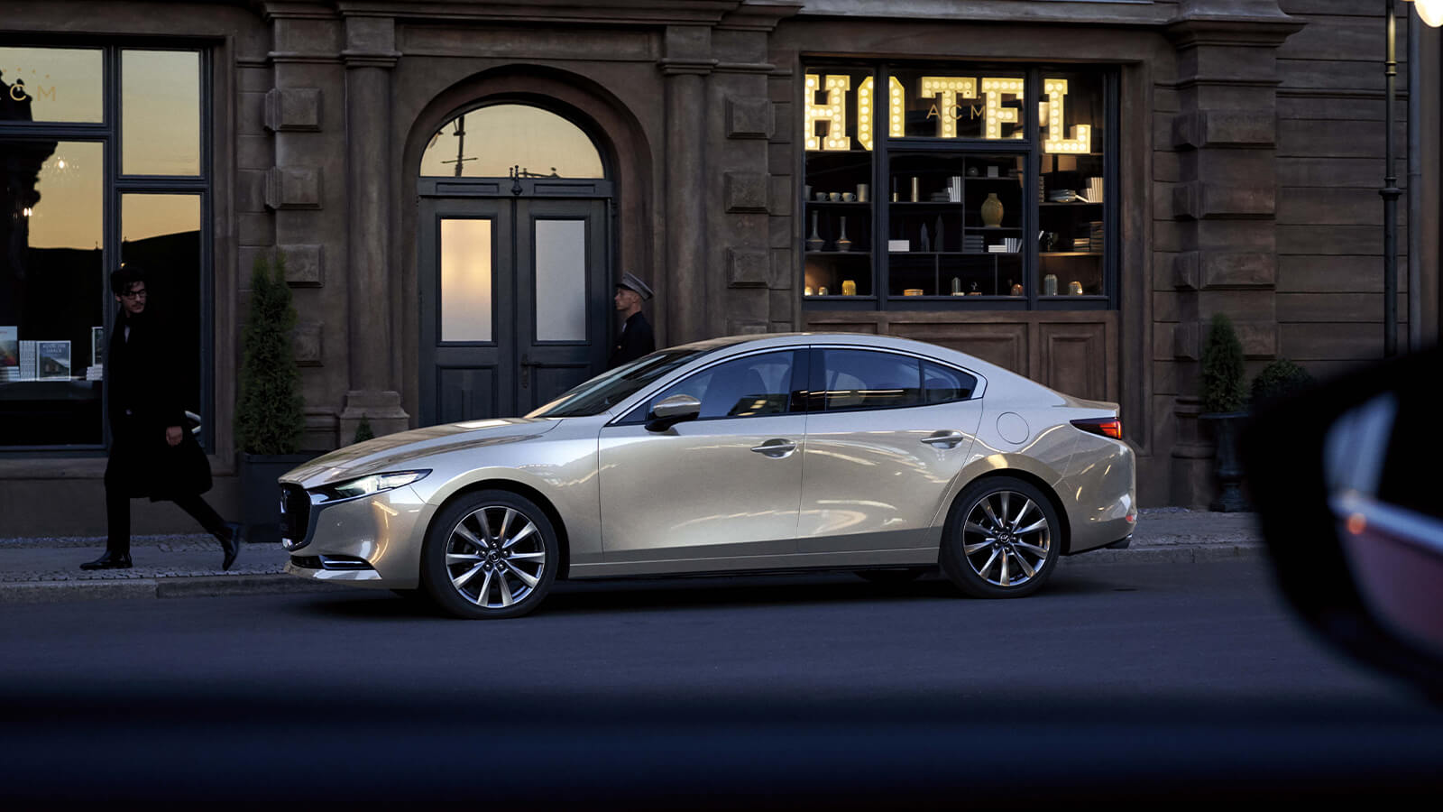 Side profile of a Platinum Quartz Metallic Mazda3 parked in front of a building.